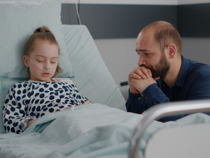 A worried father sitting beside his sick child who's in a hospital bed