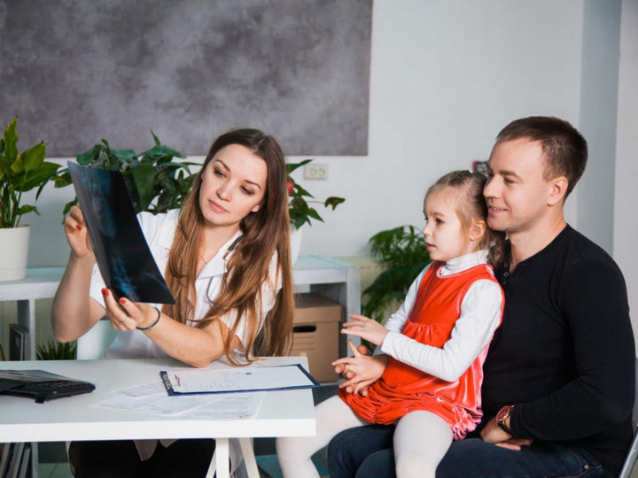A pediatrician looking at a child xray while daughter sits on her dads lap