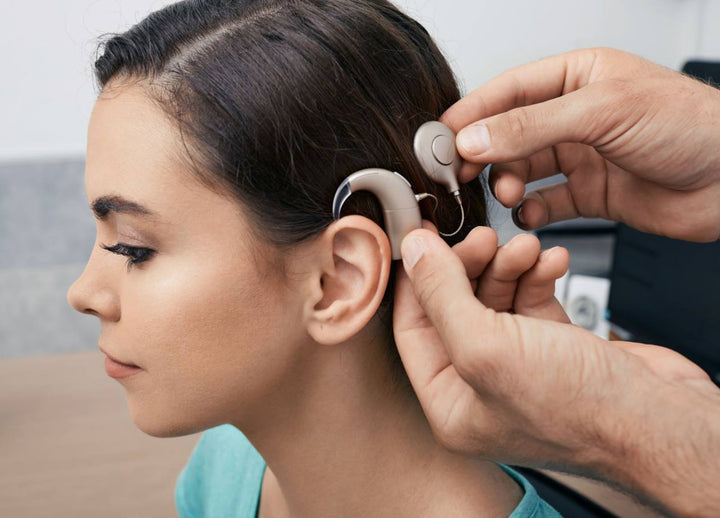 a woman seated and while man places a cochlear implant on her ear