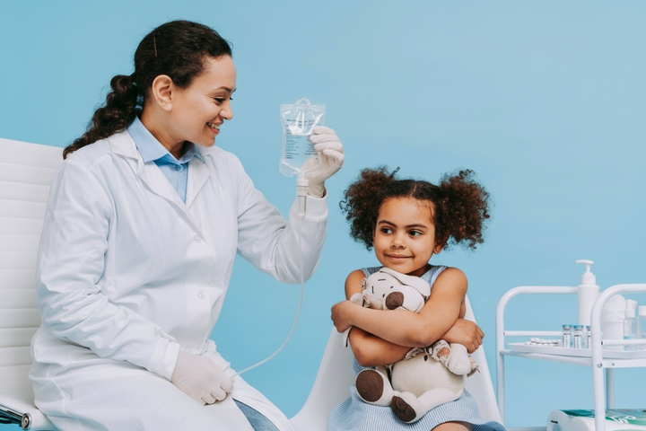 A dr holding an IV while sitting neside a little girl