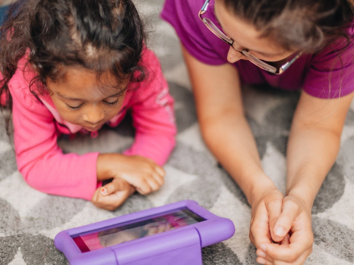 mom and daughter lie side by side while looking at AAC device