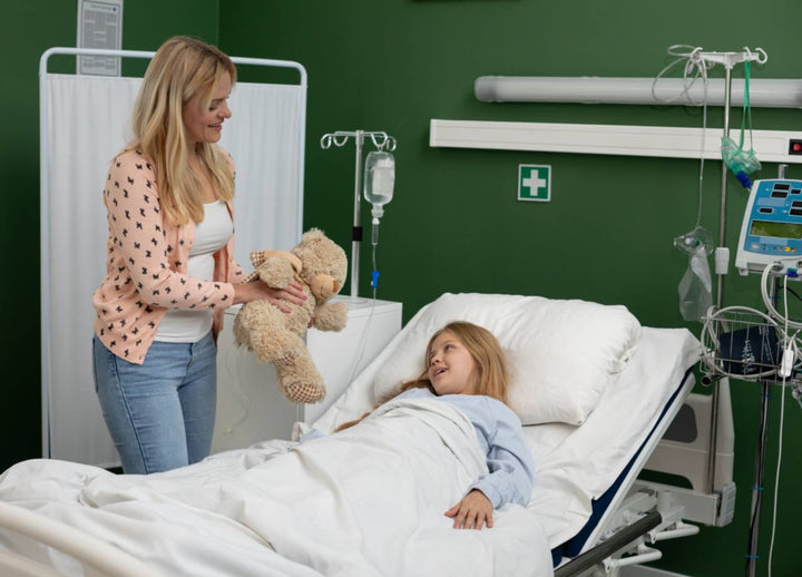 A child lying in bed with her mother handing her a fluffy teddy